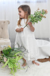 Carriage Boutique white long sleeve lace christening gown with scalloped hem worn by a toddler holding flowers