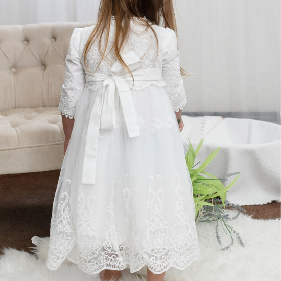 Carriage Boutique white long sleeve lace christening gown with scalloped hem and back bow detail on a young girl