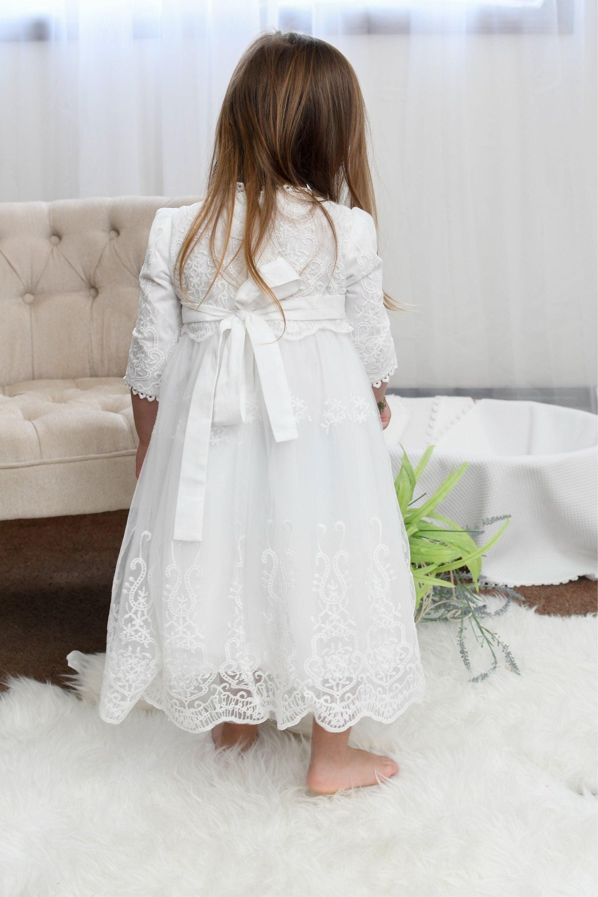 Carriage Boutique white long sleeve lace christening gown with scalloped hem and back bow detail on a young girl