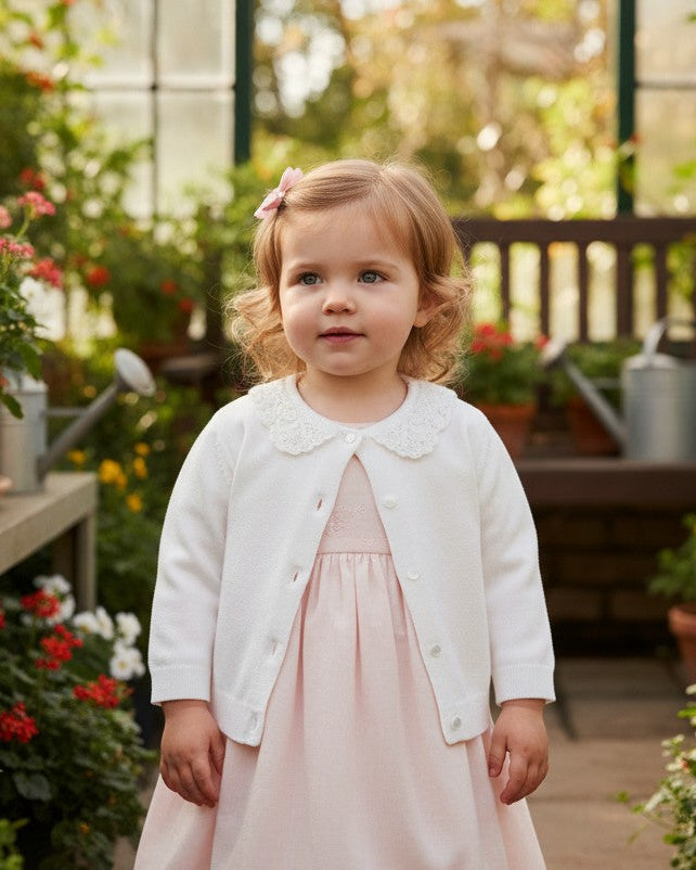 Carriage Boutique white cotton cardigan for girls featuring a delicate lace collar, worn over a soft pink dress.