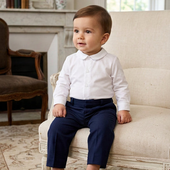 Carriage Boutique baby boy wearing a long sleeve white button-down shirt with a classic collar and navy trousers