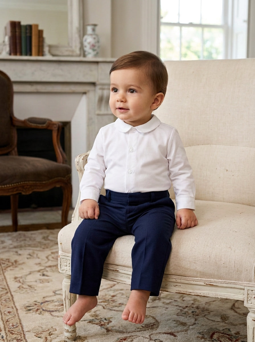 Carriage Boutique baby boy wearing a long sleeve white button-down shirt with a classic collar and navy trousers