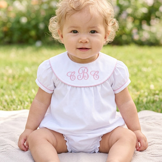 Carriage Boutique white cotton baby bubble with pink monogram embroidery and flutter sleeves on a seated toddler