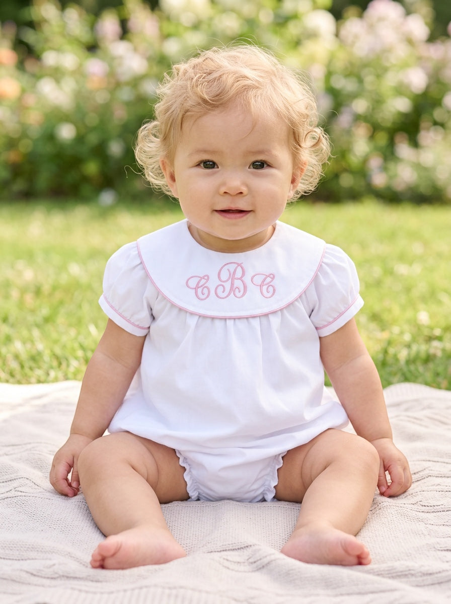 Carriage Boutique white cotton baby bubble with pink monogram embroidery and flutter sleeves on a seated toddler