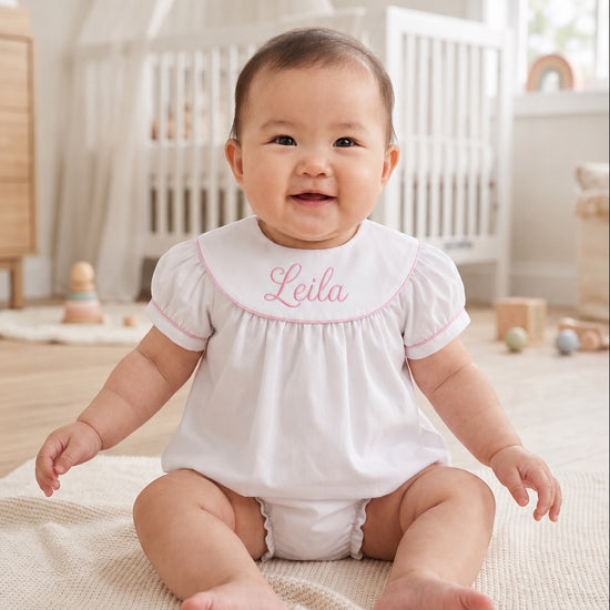 Carriage Boutique white cotton baby bubble with pink monogram embroidery and flutter sleeves on a smiling baby girl