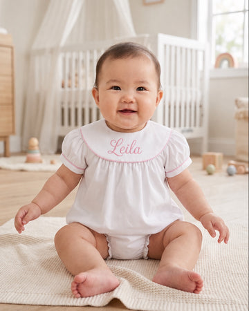 Carriage Boutique white cotton baby bubble with pink monogram embroidery and flutter sleeves on a smiling baby girl