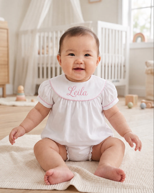 Carriage Boutique white cotton baby bubble with pink monogram embroidery and flutter sleeves on a smiling baby girl