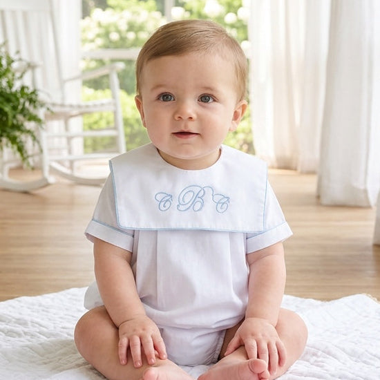 Carriage Boutique baby boy wearing a white cotton romper with blue trim and custom monogram embroidery