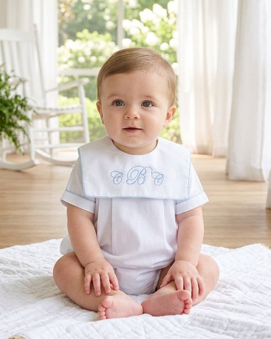 Carriage Boutique baby boy wearing a white cotton romper with blue trim and custom monogram embroidery