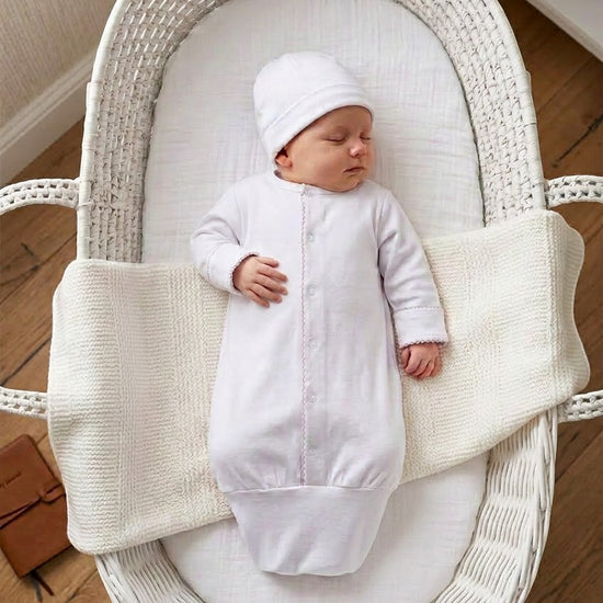 Carriage Boutique newborn sleep sack and matching hat in white with scalloped trim, worn by a sleeping baby in a bassinet