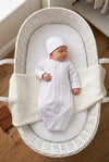 Carriage Boutique newborn sleep sack and matching hat in white with scalloped trim, worn by a sleeping baby in a bassinet