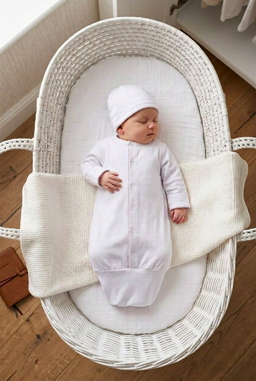 Carriage Boutique newborn sleep sack and matching hat in white with scalloped trim, worn by a sleeping baby in a bassinet