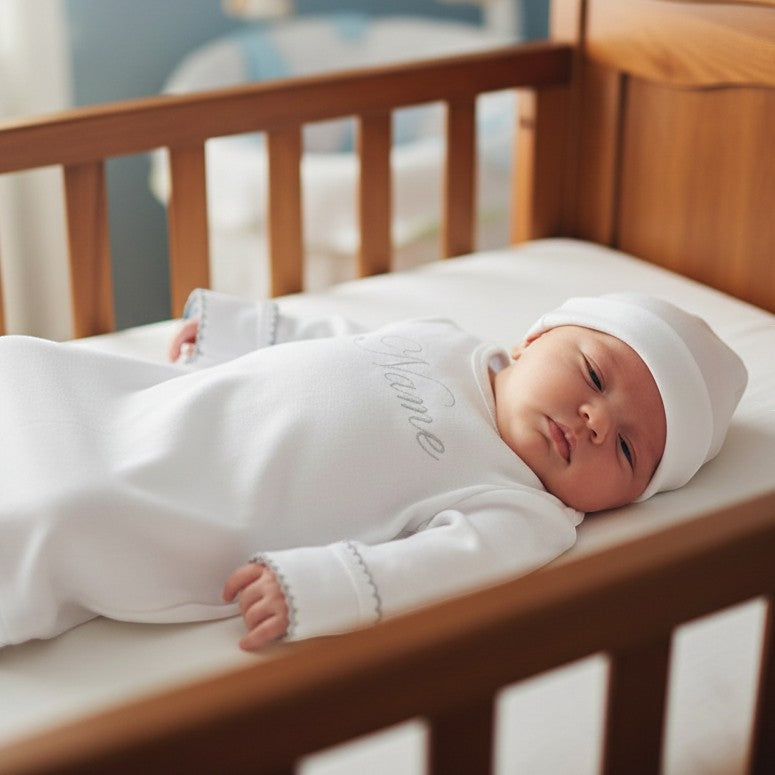Carriage Boutique white newborn sleep sack with matching hat and monogrammed name, featuring elegant scalloped trim.