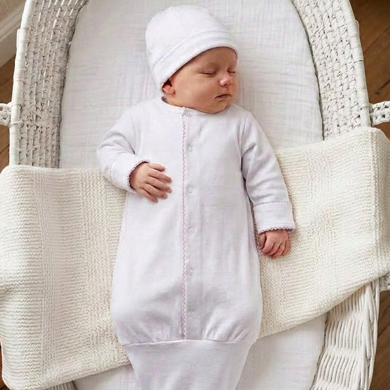 Carriage Boutique white newborn sleep sack with matching hat and scalloped trim, worn by a sleeping baby in a bassinet.