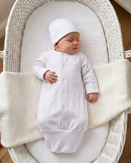 Carriage Boutique white newborn sleep sack with matching hat and scalloped trim, worn by a sleeping baby in a bassinet.