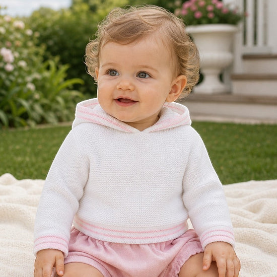Carriage Boutique baby girl wearing a white hooded sweater with pink trim and matching pink shorts outdoors.