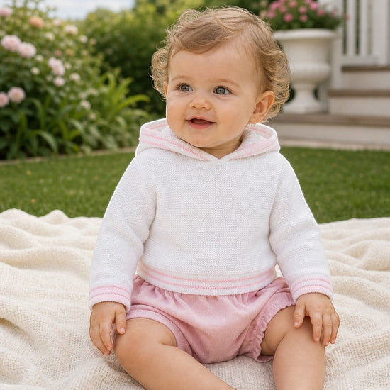 Carriage Boutique baby girl wearing a white hooded sweater with pink trim and matching pink bloomers on a blanket.