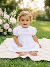 Carriage Boutique white and pink short sleeve toddler dress with personalized embroidery sitting on a garden blanket