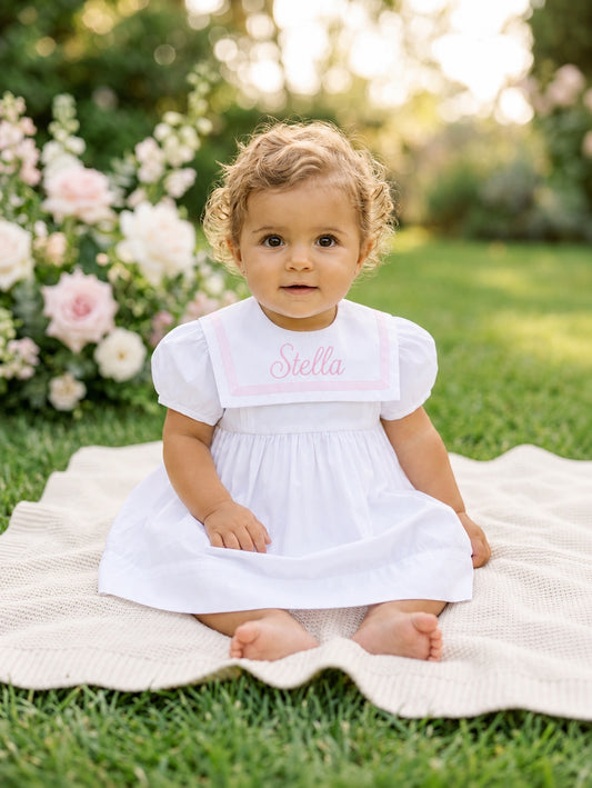 Carriage Boutique white and pink short sleeve toddler dress with personalized embroidery sitting on a garden blanket