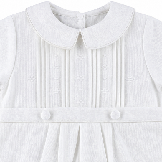 Carriage Boutique white pique baby boy romper featuring a Peter Pan collar, pleated front, and decorative buttons.