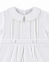 Carriage Boutique white pique baby boy romper featuring a Peter Pan collar, pleated front, and decorative buttons.