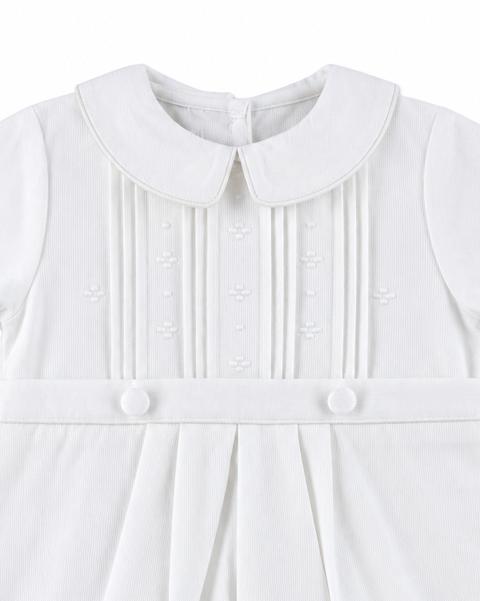 Carriage Boutique white pique baby boy romper featuring a Peter Pan collar, pleated front, and decorative buttons.