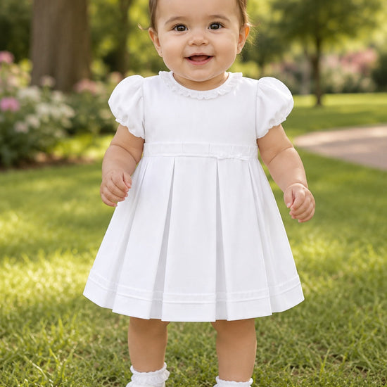 Carriage Boutique white pique toddler girl dress with puff sleeves and pleated skirt worn by a baby in a park