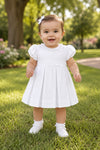 Carriage Boutique white pique toddler girl dress with puff sleeves and pleated skirt worn by a baby in a park