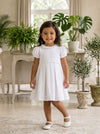 Carriage Boutique white pique toddler girl dress with puff sleeves and ruffled collar in a bright living room