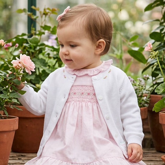 Carriage Boutique white cotton cashmere baby girl cardigan with delicate rosebud embroidery worn over a pink dress