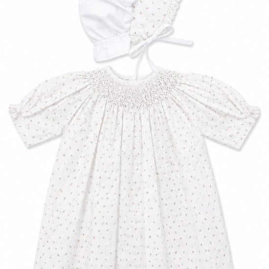 Carriage Boutique white baby girl dress with delicate rosebud print, smocked bodice, and matching lace-trimmed bonnet.