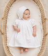 Carriage Boutique baby girl in a white rosebud print dress and matching bonnet lying in a woven wicker bassinet