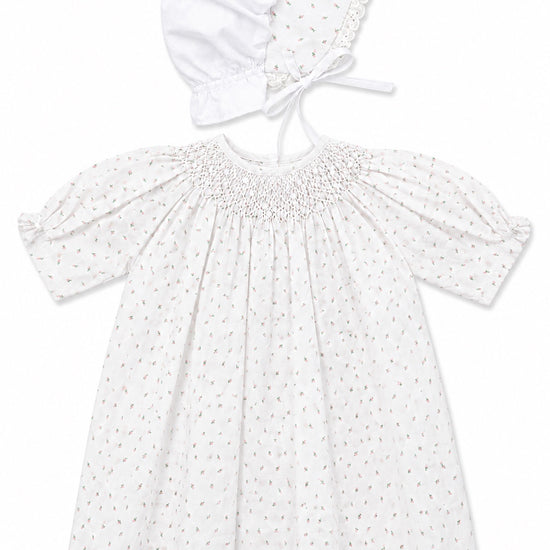 Carriage Boutique white newborn girl dress with delicate rosebud print, smocked bodice, and matching lace-trim bonnet.