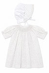 Carriage Boutique white newborn girl dress with delicate rosebud print, smocked bodice, and matching lace-trim bonnet.