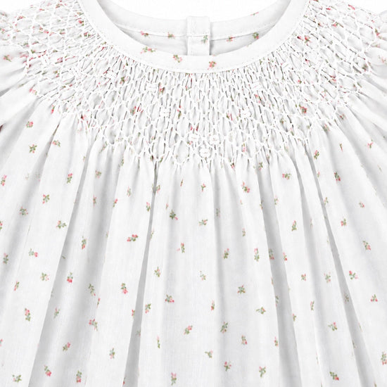 Carriage Boutique white baby girl dress featuring delicate pink rosebud print and intricate hand-smocked bodice detail.