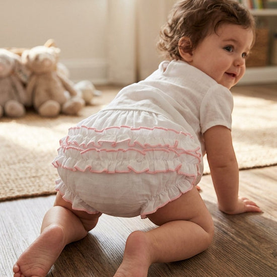 Carriage Boutique baby girl white cotton diaper cover with delicate pink ruffled trim worn by a crawling toddler
