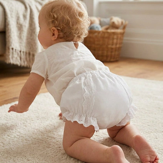 Carriage Boutique baby girl white cotton diaper cover with delicate ruffles and floral details on a crawling baby
