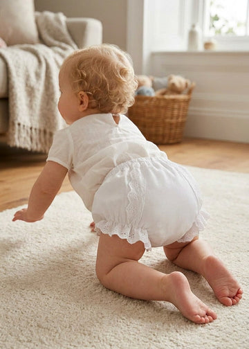 Carriage Boutique baby girl white cotton diaper cover with delicate ruffles and floral details on a crawling baby
