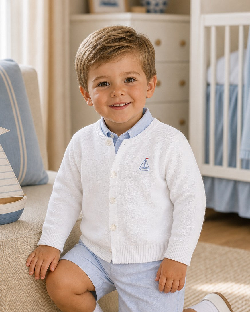 Carriage Boutique white cotton cardigan for boys featuring a small blue sailboat embroidery and button-front closure.