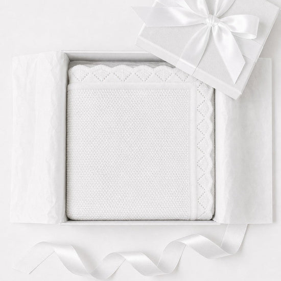 Carriage Boutique white cotton knit baby blanket with scalloped edges, presented in a gift box with a satin ribbon.