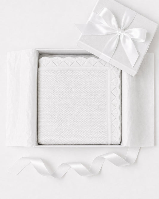 Carriage Boutique white cotton knit baby blanket with scalloped edges, presented in a gift box with a satin ribbon.