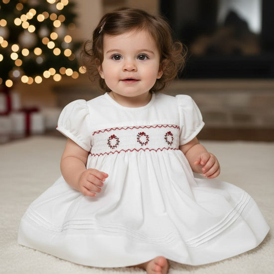 Carriage Boutique white baby dress with short sleeves, hand smocking, and red wreath embroidery for Christmas