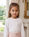 Carriage Boutique white long sleeve blouse with a ruffled smocked collar worn by a young girl with a pink hair bow.