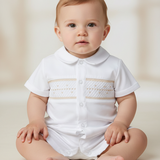 Baby boy wearing a white Carriage Boutique bobby suit with hand-smocked beige detailing for formal occasions.