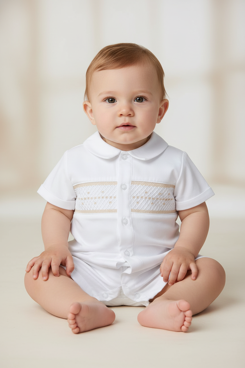 Baby boy wearing a white Carriage Boutique bobby suit with hand-smocked beige detailing for formal occasions.