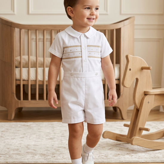 Toddler boy wearing a white Carriage Boutique hand-smocked bobby suit with shorts for a formal occasion.