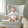 Carriage Boutique white cotton baby boy romper with hand-smocked carousel horse design and blue trim.