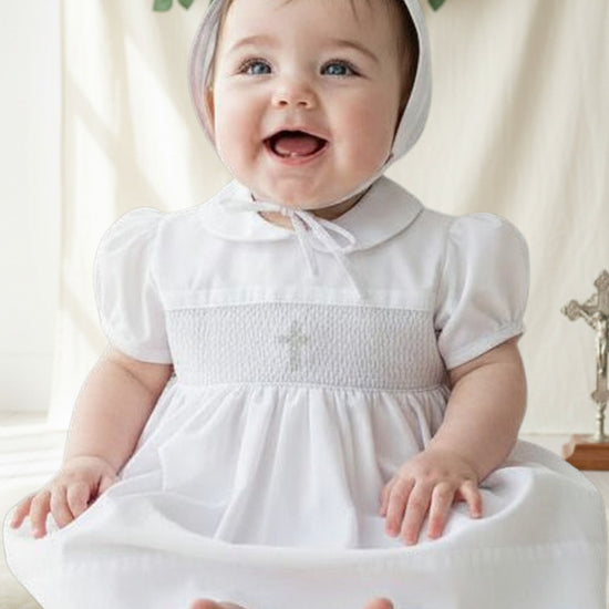 Carriage Boutique white smocked christening dress with cross detail and bonnet on a baby girl.