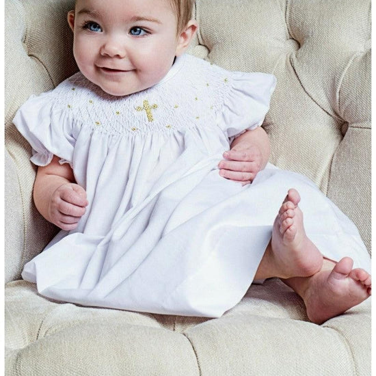 Baby girl wearing a Carriage Boutique white cotton smocked bishop dress with gold cross detail for christening