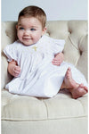 Baby girl wearing a Carriage Boutique white cotton smocked bishop dress with gold cross detail for christening